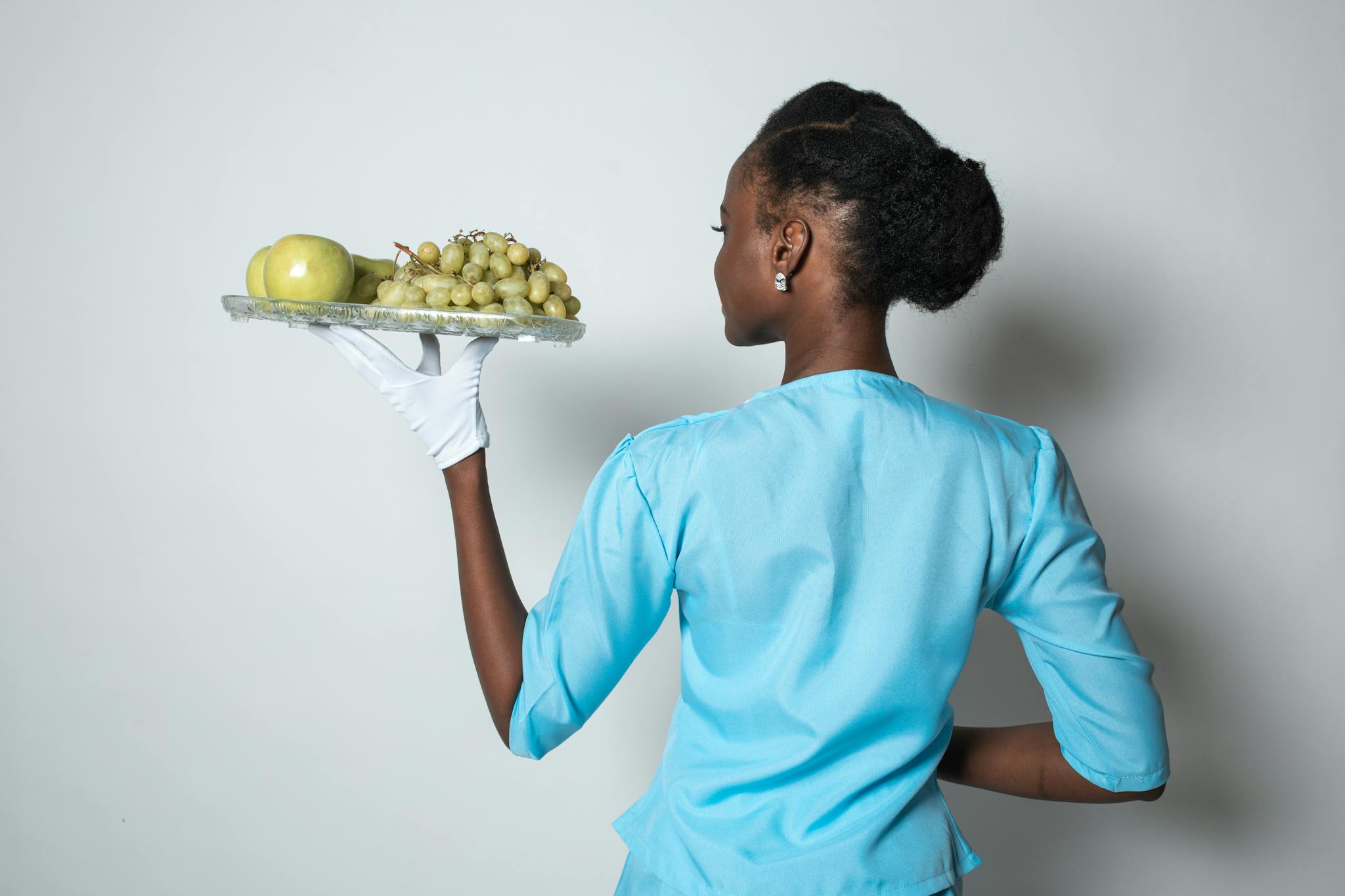 A poised woman carrying a tray with fruits, dressed in light blue with elegance.