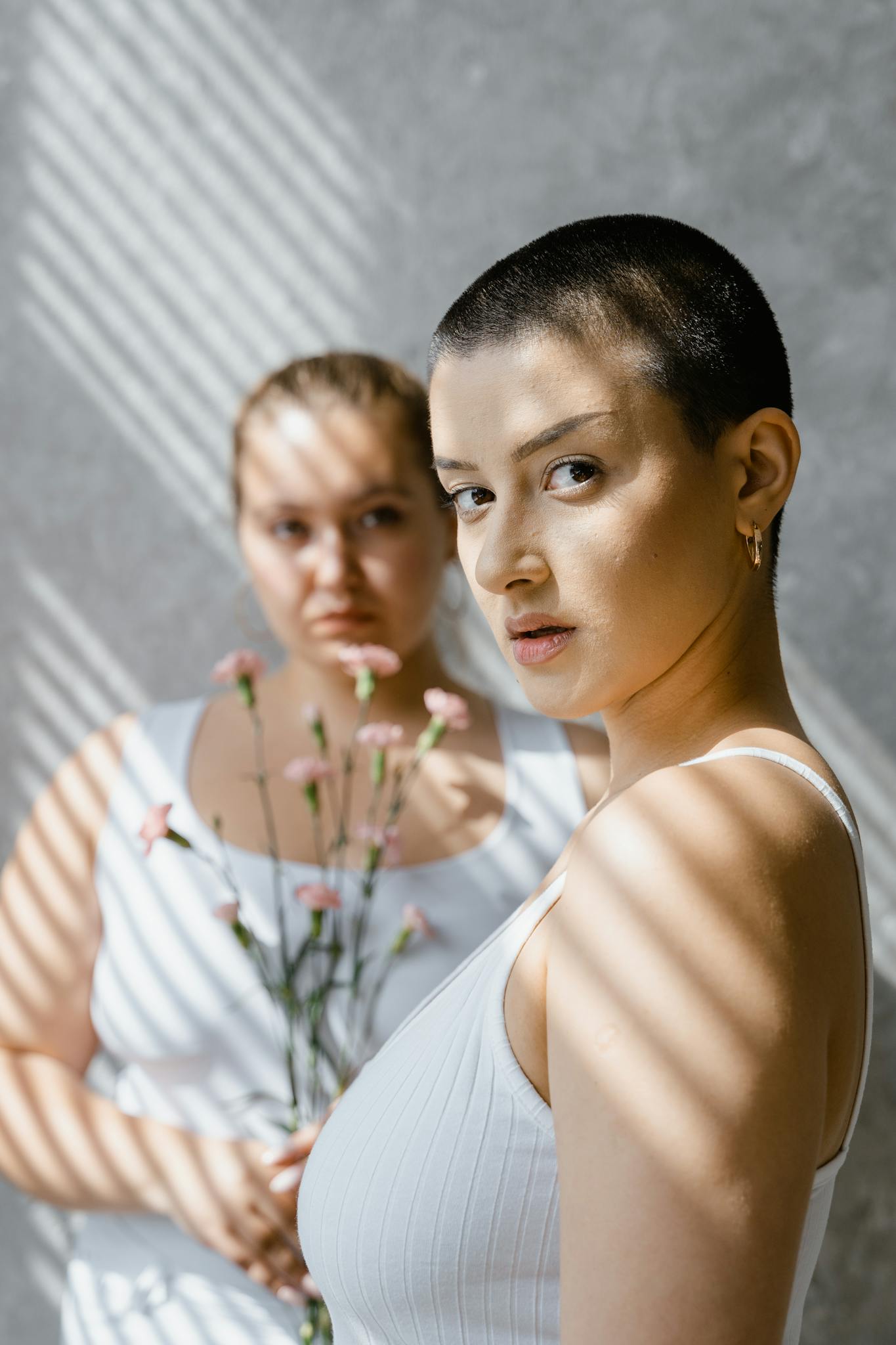 Artistic portrait of two women with flowers, accented by shadows indoors.