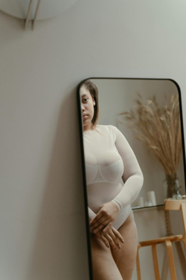 Confident woman embracing her body in a soft indoor setting, exuding self-acceptance.