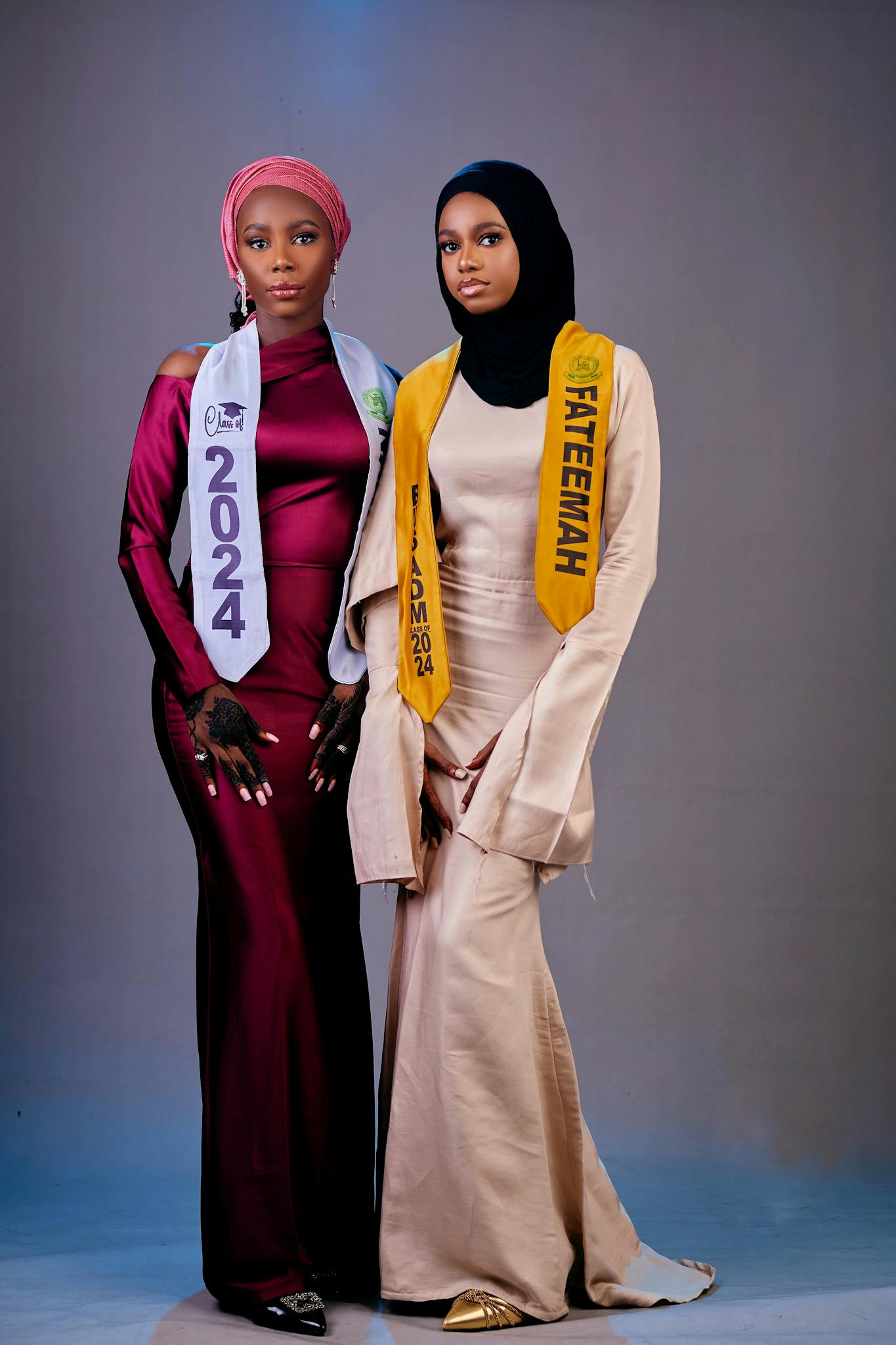 Two young women in elegant dresses and sashes posing confidently.